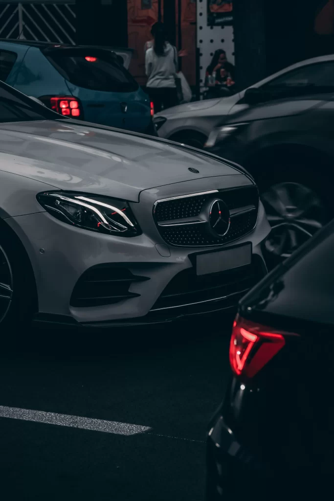 Sudrabains Mercedes-Benz automobilis starp citām automašīnām tumšā autostāvvietā