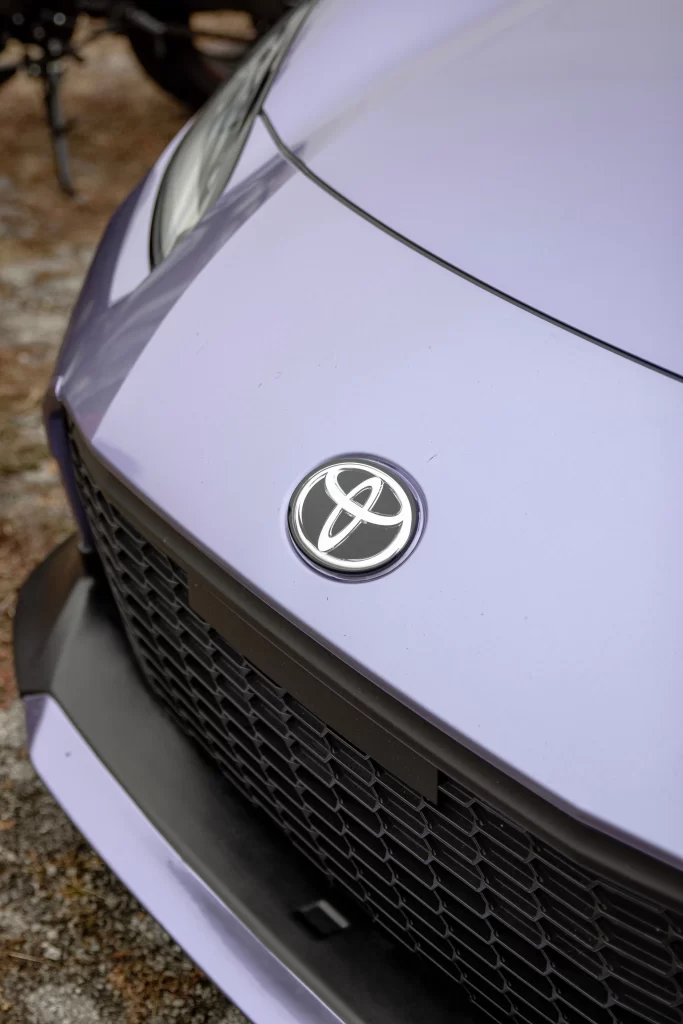 Крупный план светло-фиолетового капота Toyota с эмблемой Toyota и чёрной решёткой радиатора